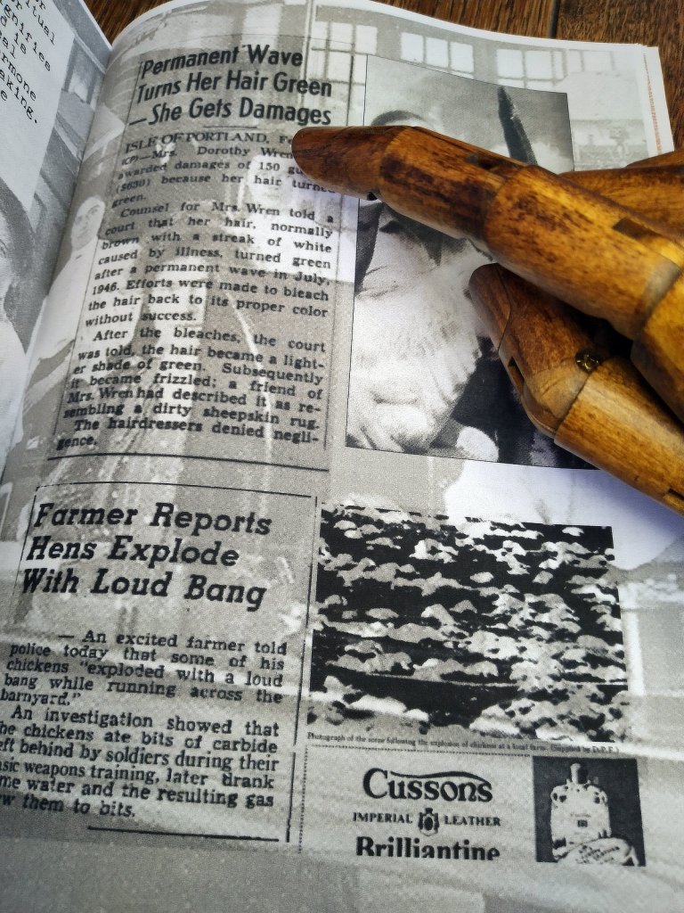 A wooden hand pointing at a page from a booklet showing items from old newspapers.